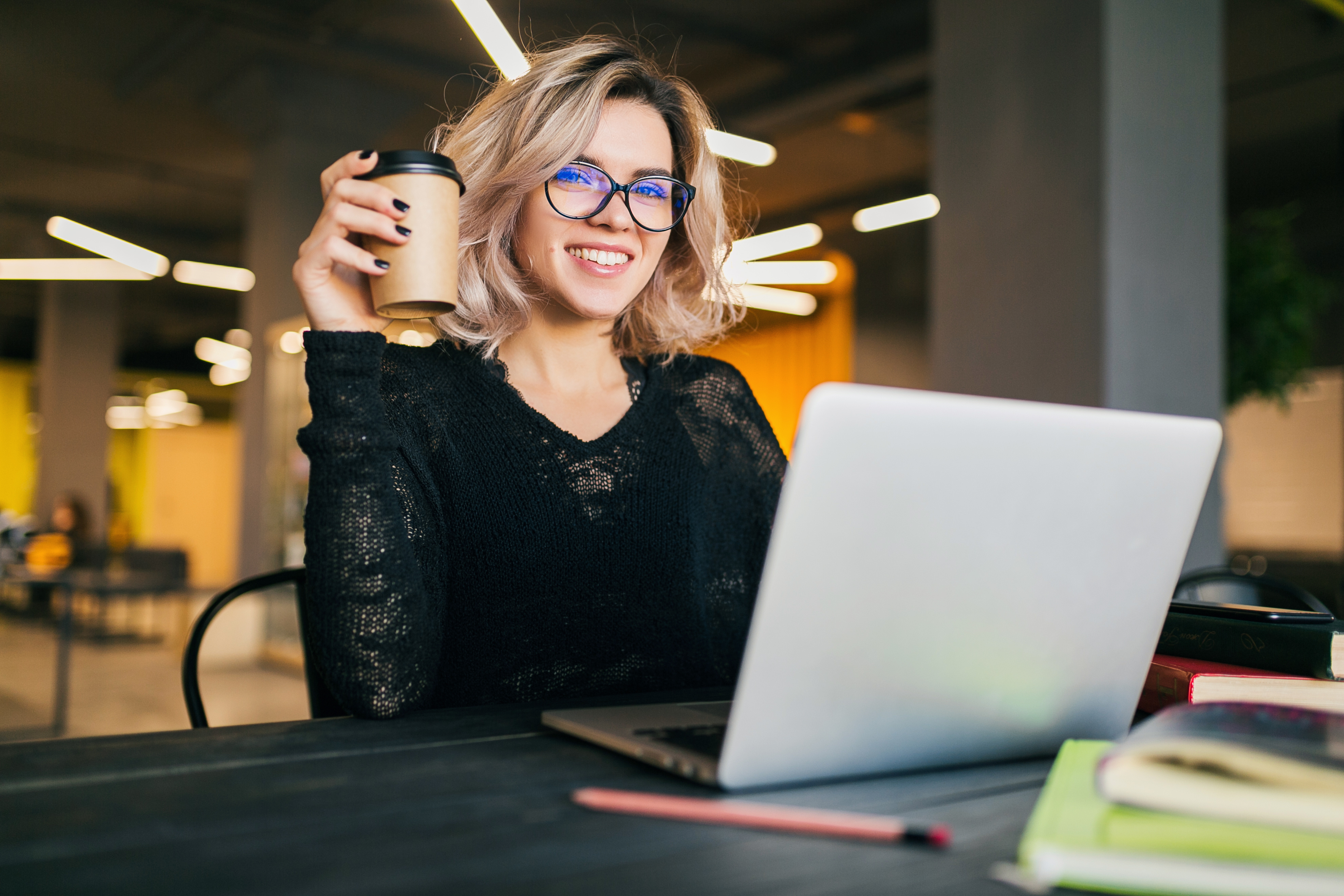 portrait-of-young-pretty-woman-sitting-at-table-in-black-shirt-working-on-laptop-in-co-working-office-wearing-glasses-smilin